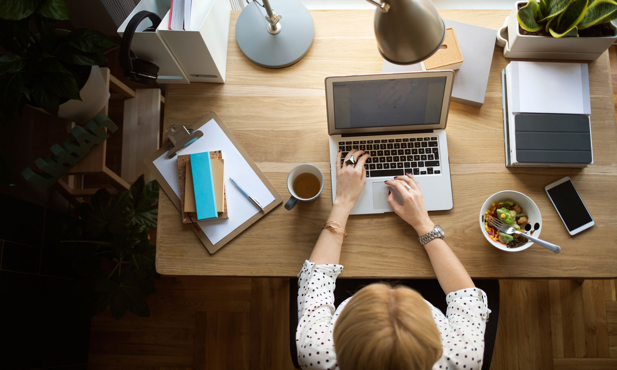 Kvinna sitter hemma på sitt kontor, jobbar på sin laptop och äter sallad
