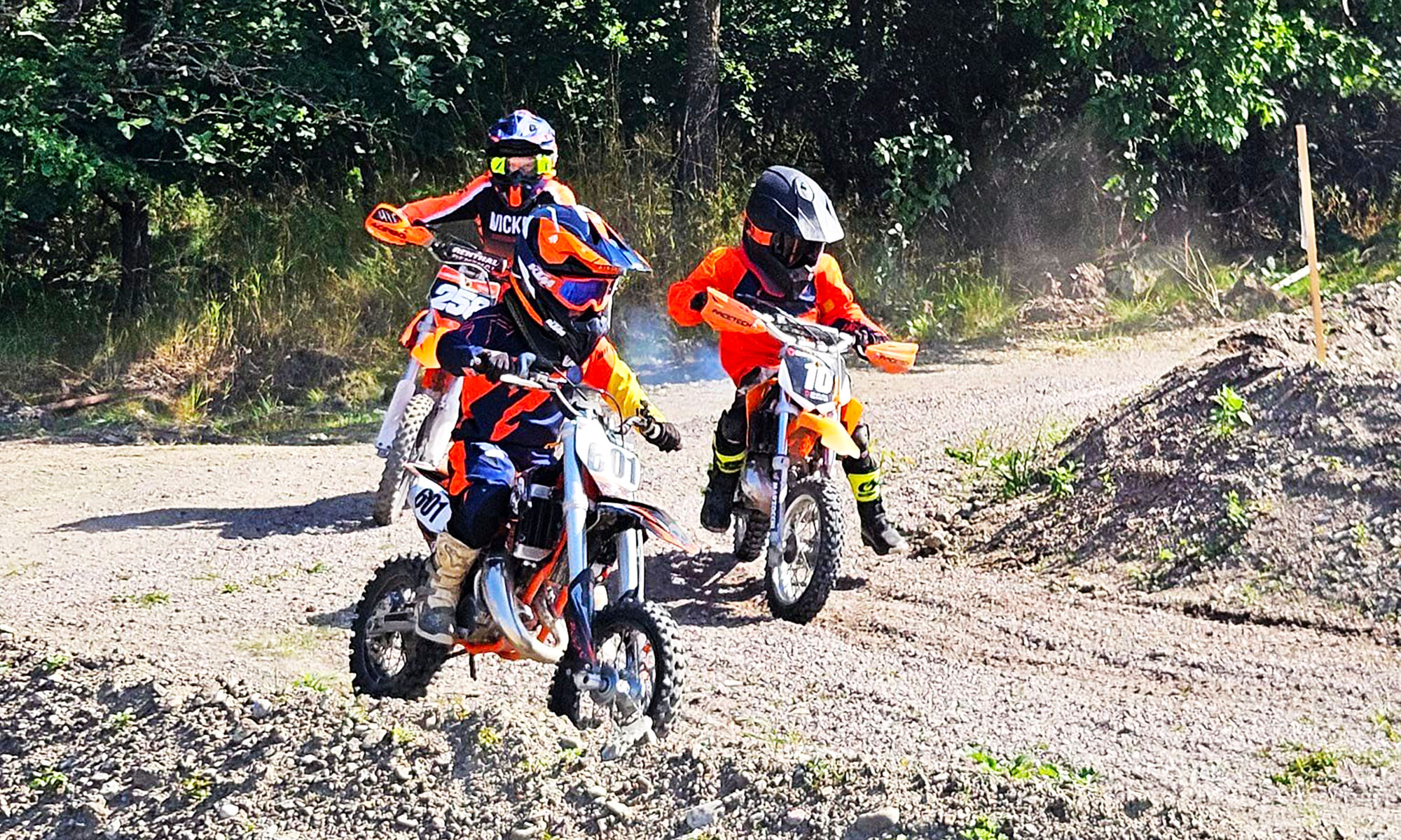 Tre barn kör crossmotorcyklar på en crossbana.